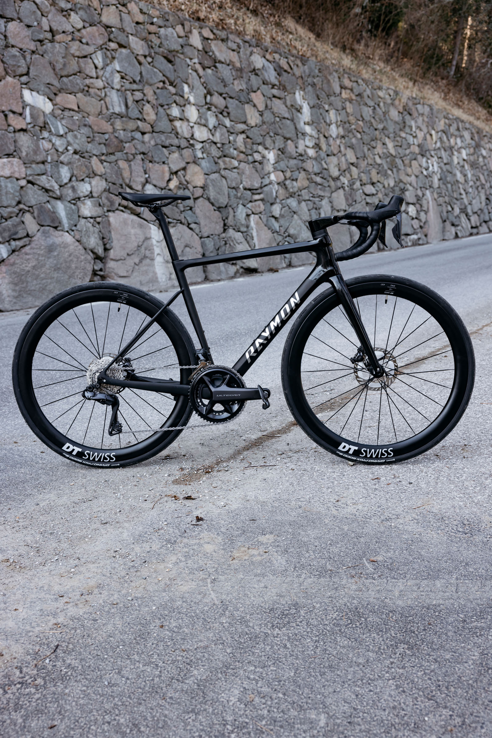 Schwarzes RAYMON-Rennrad mit DT-Swiss-Laufrädern vor einer Steinmauer